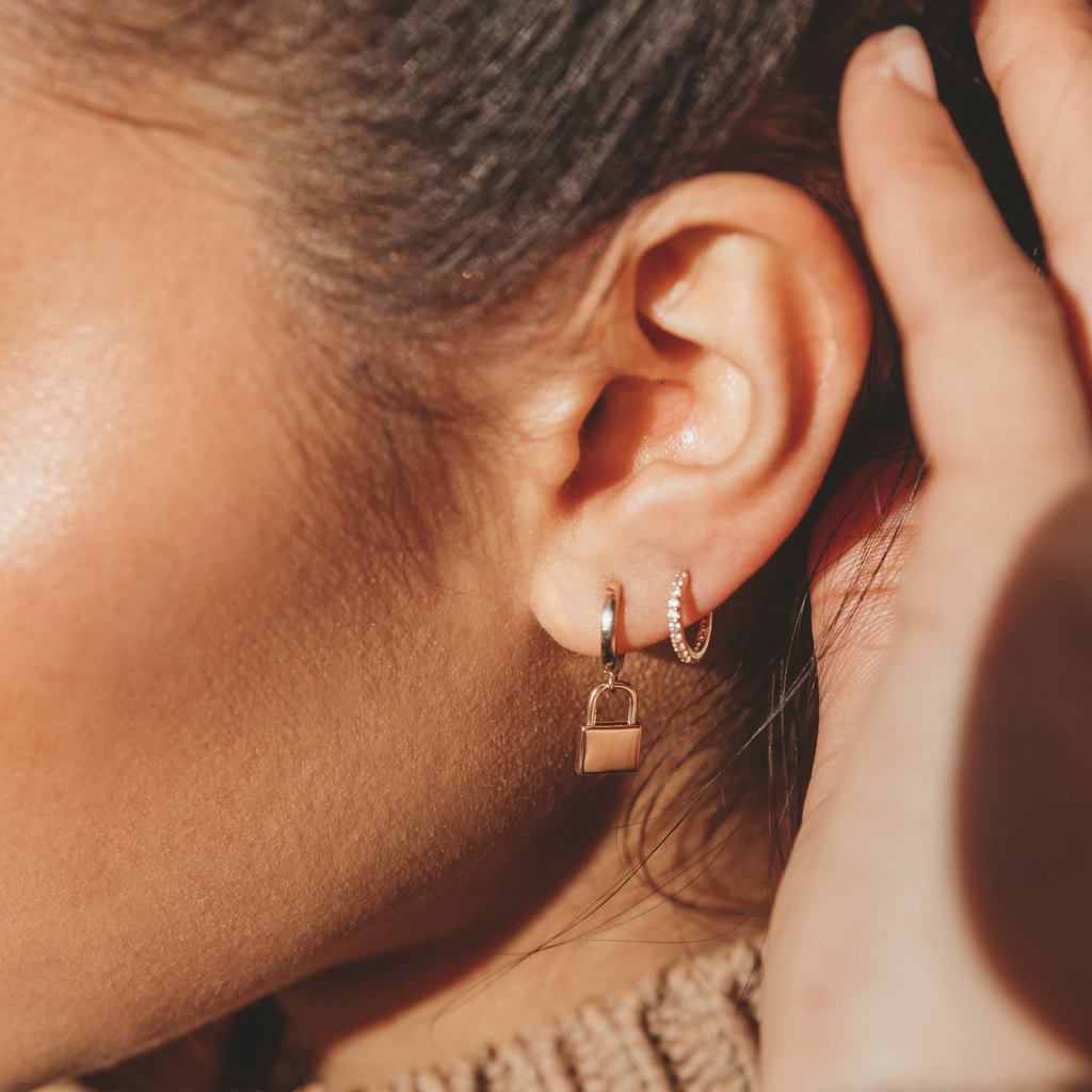 model with two earrings in, one gold padlock hoop earring and another delicate hoop earring with crystals