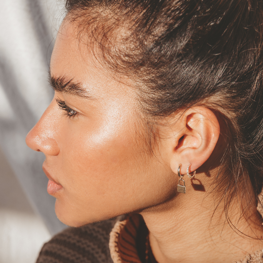 model wearing two earrings in one ear, one yellow gold padlock earring and a second huggie hoop earring with small crystals