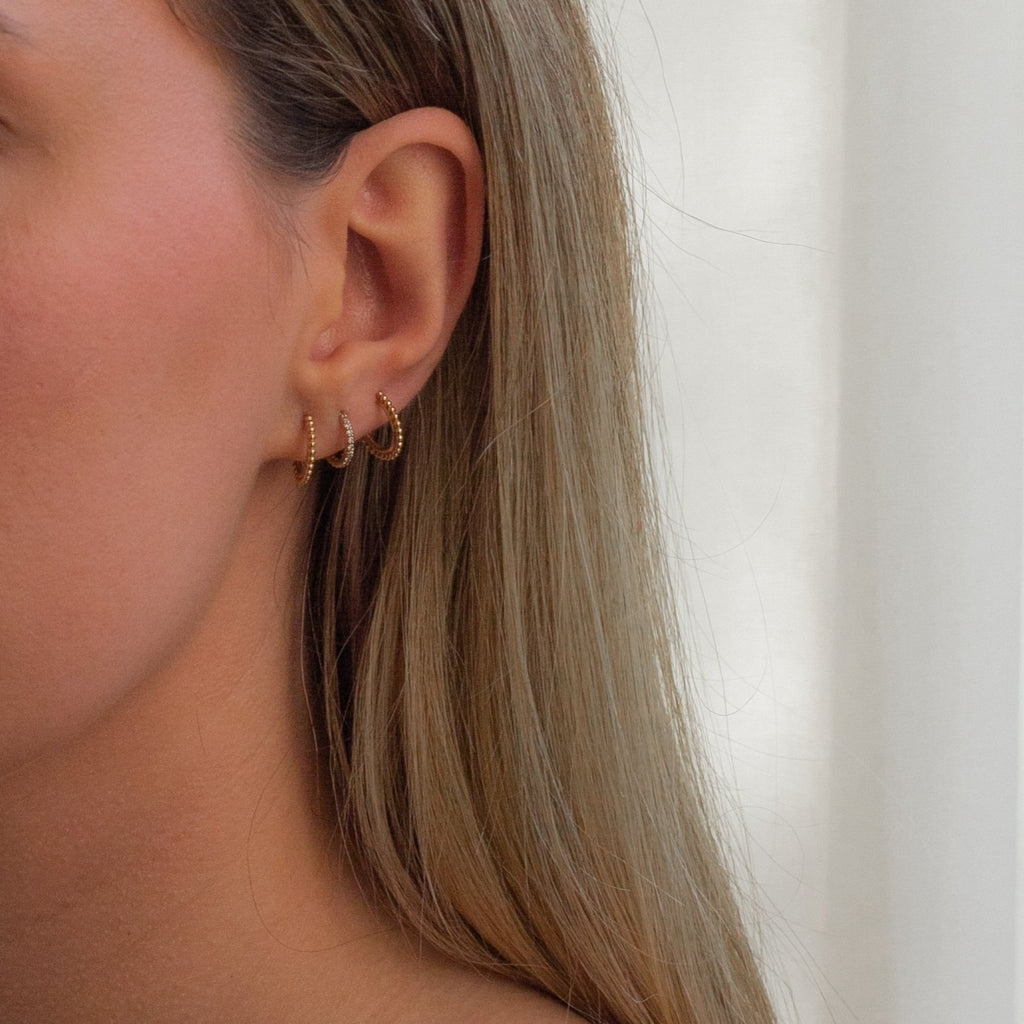 woman wearing an ear stack of three huggie hoop earrings in 18k gold